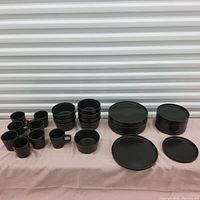 Full set of black stoneware dinnerware arranged on a surface showing coffee cups, bowls, small plates, and dinner plates in stacks.