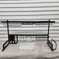 Full view of black metal oversink adjustable dish rack with assembly instructions on cloth underneath.