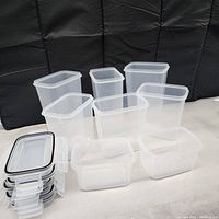 Photo showing eight clear plastic rectangular food storage containers with white snap-lock lids and black sealing rings for airtight storage. Containers grouped to display three large, three medium, and two small sizes.