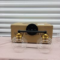 Bathroom light fixture with two clear glass globe shades displayed in front of its original box.