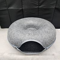 Gray donut-shaped cat play tunnel resting on light surface with a black backdrop.