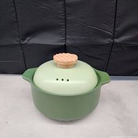 Green ceramic pot with matching lid and light wood knob with vent holes, shown on plain background.