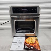 Cosori air fryer oven with digital touchscreen showing temperature, closed door, recipe book and user manual in front