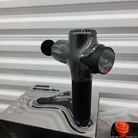 Dacorm massage gun on its product box showing carbon fiber style body and round black massage head attached.