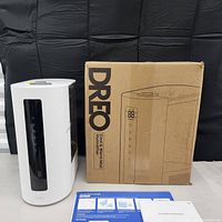 White Dreo humidifier and dehumidifier device next to original brown box and paper documentation on light surface.