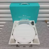 Top view of the white Lefant robot vacuum cleaner inside packaging, showing the main device and accessories beside it in molded foam.