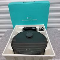 Open box showing black Lefant robot vacuum cleaner unit inside foam packaging, with charging base and remote control next to it.