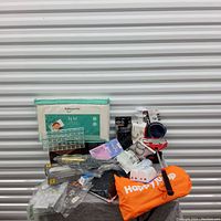 Photo showing assorted household and personal care items including Babyworks branded disposable bed sheet, Happy Jumper orange bag, hair nets, electric lighter, nail files, earbuds, and other small items.