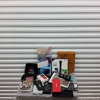 Mixed lot items including physical media, phone cases, a keyboard, electronic device packaging, and accessories arranged on a small table.