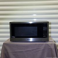 Front view of Panasonic stainless steel microwave on fabric-draped table with corrugated metal background.