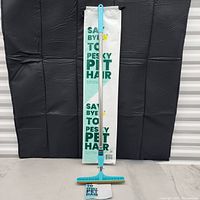 Photo of the telescopic pet hair collector standing upright in front of its branded packaging bag marked 'Say Bye To Pesky Pet Hair'.