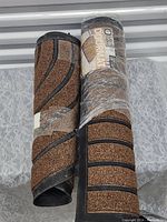 Two rolled door mats, one partially unrolled showing brown coir surface with black rubber pattern striping.