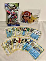 Photo showing a sealed pack of Pokémon cards alongside assorted loose Pokémon trading cards and a lenticular image of Pikachu and Ash.