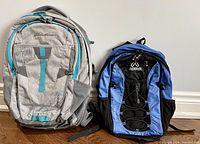 Two backpacks side by side; Eddie Bauer grey backpack with turquoise accent and Asolo blue and black backpack