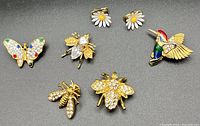 Top-down view of all brooches and earrings showing clear details of crystal and enamel accents on bees, bird, butterfly, and daisies.