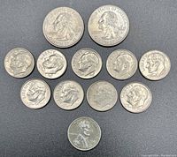 Top-down image showing 13 assorted US coins from 1943 to 2005 including quarters, dimes, nickels, and pennies arranged on a gray surface.