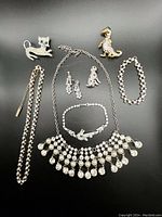 Full view of collection laid out on black surface showing the necklaces, bracelets, brooches, and earrings with sparkling clear crystals.