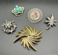 Overview of five costume brooches on black background showing different styles and materials