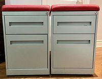Front view of two small metal filing cabinets with red cushioned tops, showing drawer handles and keyholes