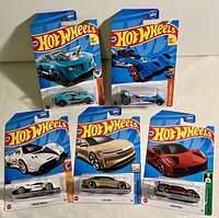 Photo showing all six Hot Wheels cars in original packaging on blue and yellow backing cards, including the Twinduction model and others in various colors.