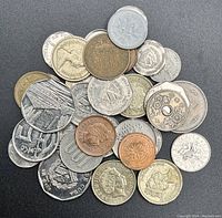 Top view of various international circulated coins showing detailed engravings, different metals, and sizes on a black background.
