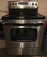 Front view of the stainless steel Maytag electric stove showing the control panel, cooktop, and oven door with window.