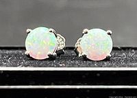 Close-up front view of the pair of silver 925 stud earrings with lab-created fire opal stones on a black surface.