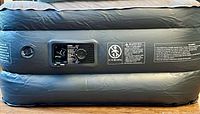 Section of grey inflatable air bed showing built-in valve and warning labels