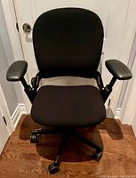 Front view of Steelcase black fabric office chair with padded armrests on caster wheels.