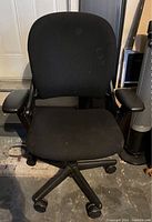 Front view of black Steelcase office chair showing padded seat and armrests on caster wheels.