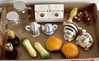Box containing various vintage salt and pepper shakers arranged to show different styles, colors and shapes including cats, birds, fruits and bottles.