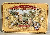 Top view of the vintage La Cure Gourmande cookie tin showing detailed French village artwork and branding.