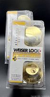 Photo showing two new brass-colored Weiser Lock Elements Series Security Deadbolts in original packaging with keys.