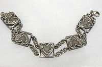 Close-up view of linked heart-shaped plaques engraved with 'ANAM CARA' and lobster claw clasp on silver-tone chain bracelet.