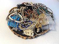 Overview of assorted costume jewelry on a black circular display base showing bracelets, necklaces, and earrings of various beads, materials and colors.