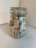 Front view of glass jar filled with small bundles of varied Spanish stamps