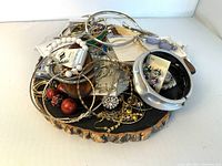Top-down photo of assortment of costume jewelry items placed on a round wood slice, including bangles, earrings, and necklaces all tangled together.