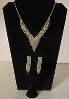 V-neck rhinestone necklace with matching earrings displayed on a black mannequin bust. Necklace shows the detailed V-shaped design formed by rhinestones and matching earrings with multiple dangling strands.