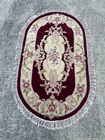 Full view of the Royal Palace oval wool rug showing its antique burgundy color, floral border design, and fringe