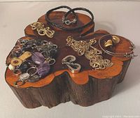 Variety of jewelry displayed on wood base showing necklaces, bracelets, earrings in gold and silver tones with mixed materials
