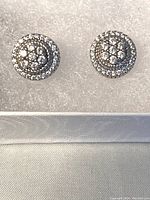 Pair of sterling silver cubic zirconia stud earrings displayed on soft white cushion inside jewelry box.