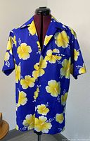Front view of vintage blue cotton Hawaiian shirt with large yellow hibiscus flowers, button front, short sleeves, and chest pocket.