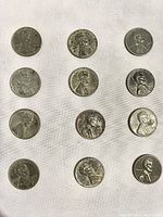 Obverse side of twelve 1943 steel pennies laid out on white fabric, showing Lincoln's profile with noticeable wear.