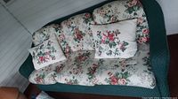 Full view of green wicker sofa with floral cushions and pillows