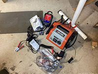 Overview of Black & Decker battery charger, Duralast maintainer, cables, and user manual spread on floor.