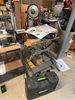 Bauer bandsaw mounted vertically on a metal stand with a wooden handle, manuals on top and hard plastic case on floor
