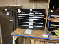 Black Craftsman 5 drawer tool box on bench with labels and tags visible