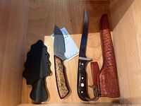 Photo of two custom fixed blade knives side by side, one with a black plastic sheath and the other with a brown leather sheath