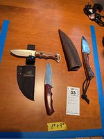 Three fixed-blade cutters and two sheaths on wooden surface, showing sizes 8 to 9 inches.