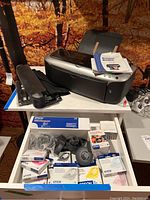 White drawer unit drawer opened showing Epson ink cartridges in original packaging, printer parts, and photo paper